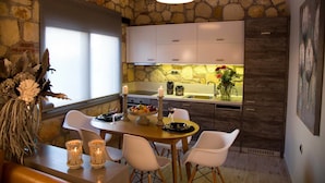 Una cocina de paredes de piedra con armarios blancos, una mesa de comedor con sillas y vistas al área de la cocina.