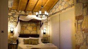 Un dormitorio con pared de piedra, techo de madera, cama con dosel, lámparas de noche y un ventanal con persianas.