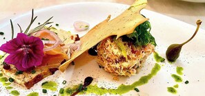 A plate with a variety of food items including a piece of bread, a flower, and a green sauce. - Hotel-Restaurant Le Cigalon (Waldbillig)