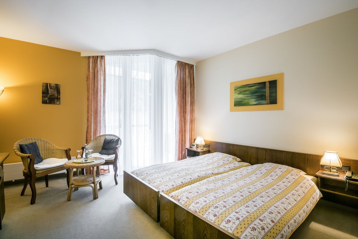 Ein Hotelzimmer mit einem Bett, zwei Stühlen, einem kleinen Tisch, einem Nachttisch und einem Bild an der Wand.