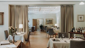 A hotel dining area with tables set for two, a bar area with bottles, and a view of the dining room through a doorway. - Hotel-Restaurant Le Cigalon (Waldbillig)