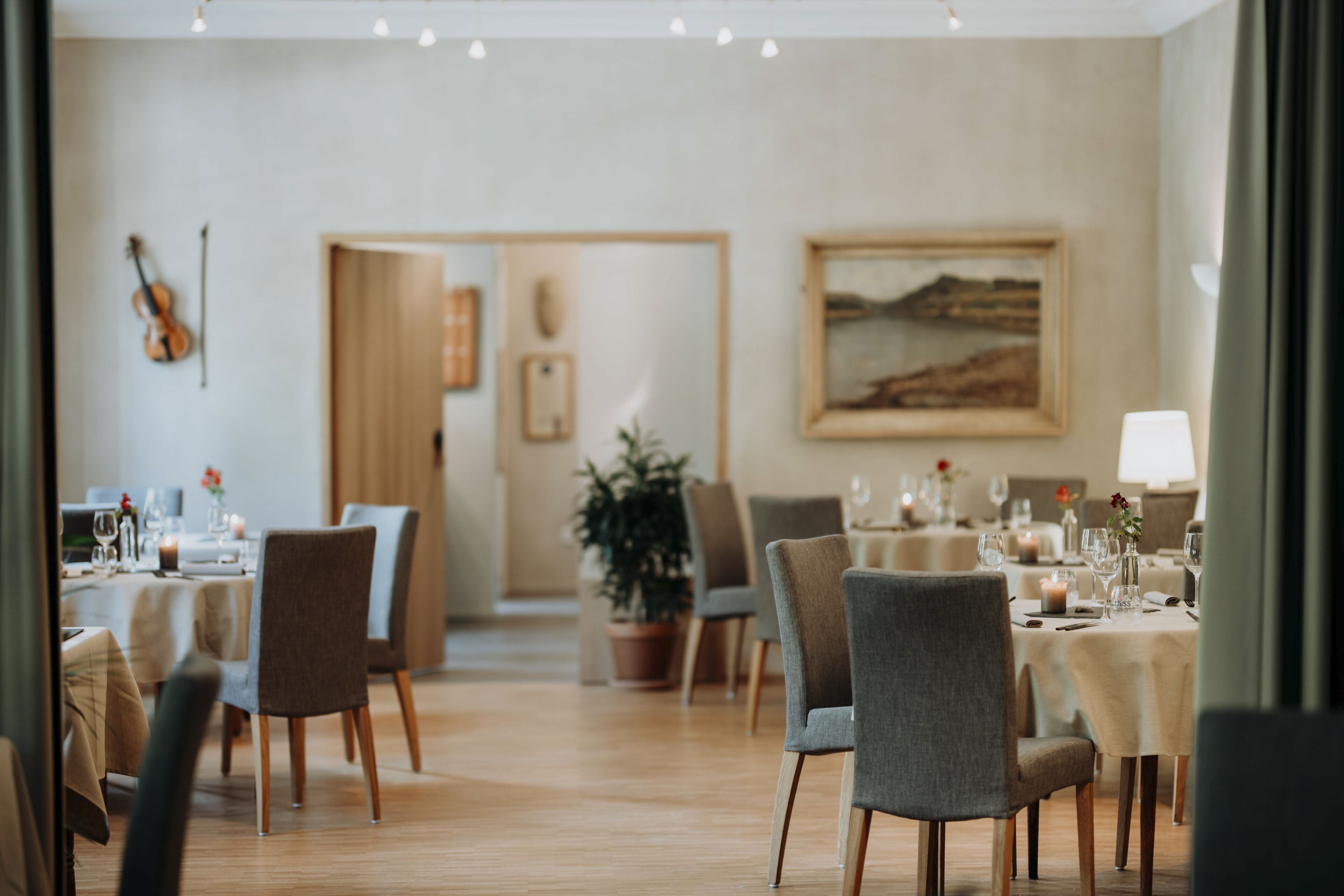 A dining area with tables set for a meal, chairs, a violin on the wall, and a painting on the wall.