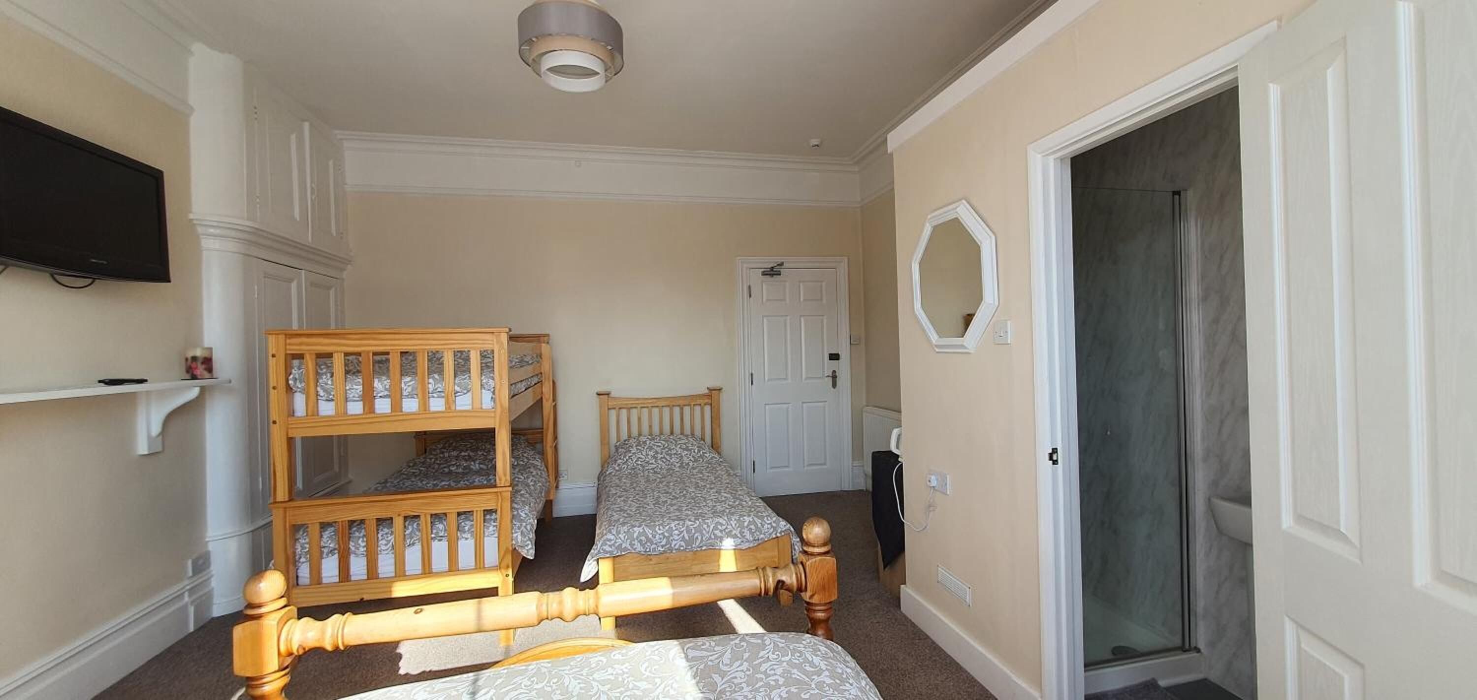 A bedroom with bunk beds, a door, a mirror, and a television on the wall.