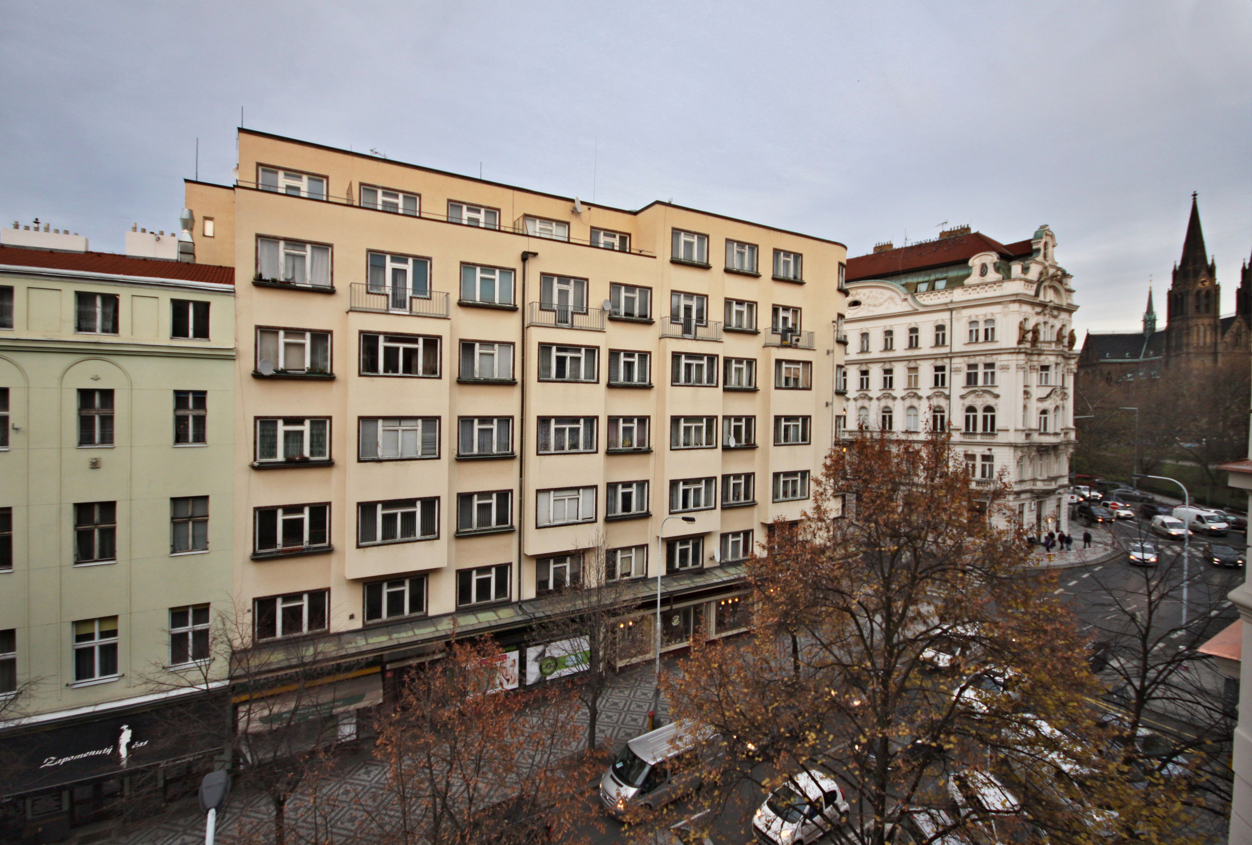 A multi-story building with a row of windows and balconies, adjacent to a historic building with a pointed tower.