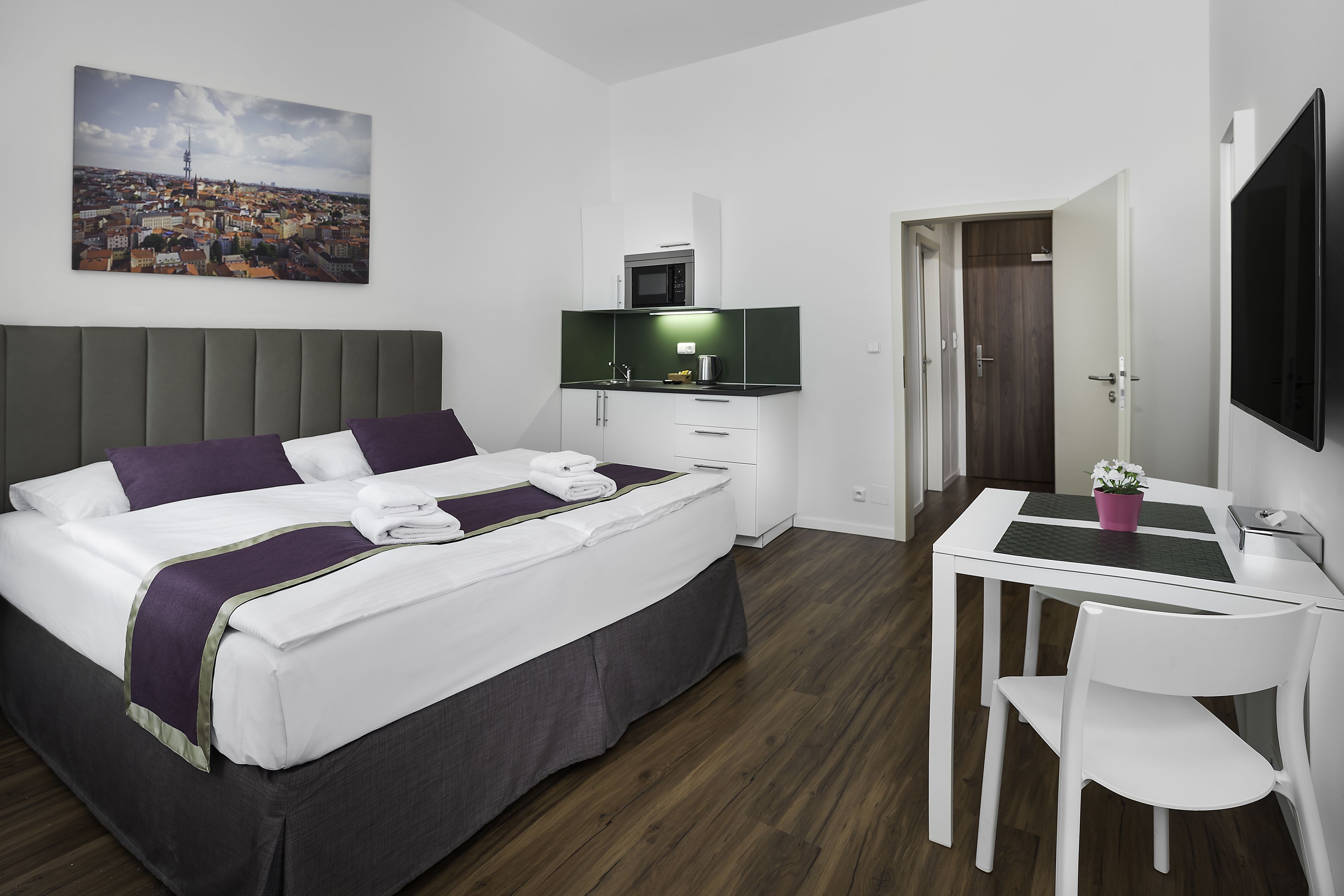 A hotel room with a bed, a desk, a chair, a TV, and a painting on the wall.