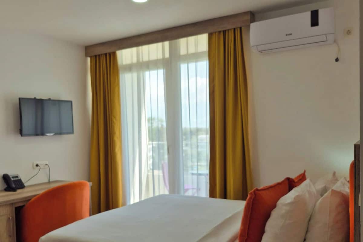 Een hotelkamer met een bed, een bureau met stoel, een televisie en een airconditioning.