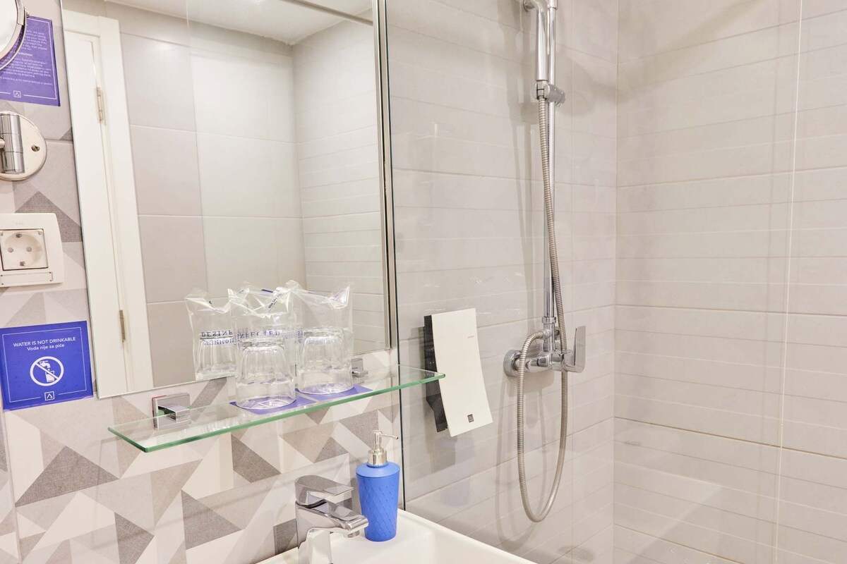 Ein modernes Badezimmer mit Duschkabine aus Glas, einem weißen Waschbecken und einem Spiegel sowie einem gemusterten Boden.