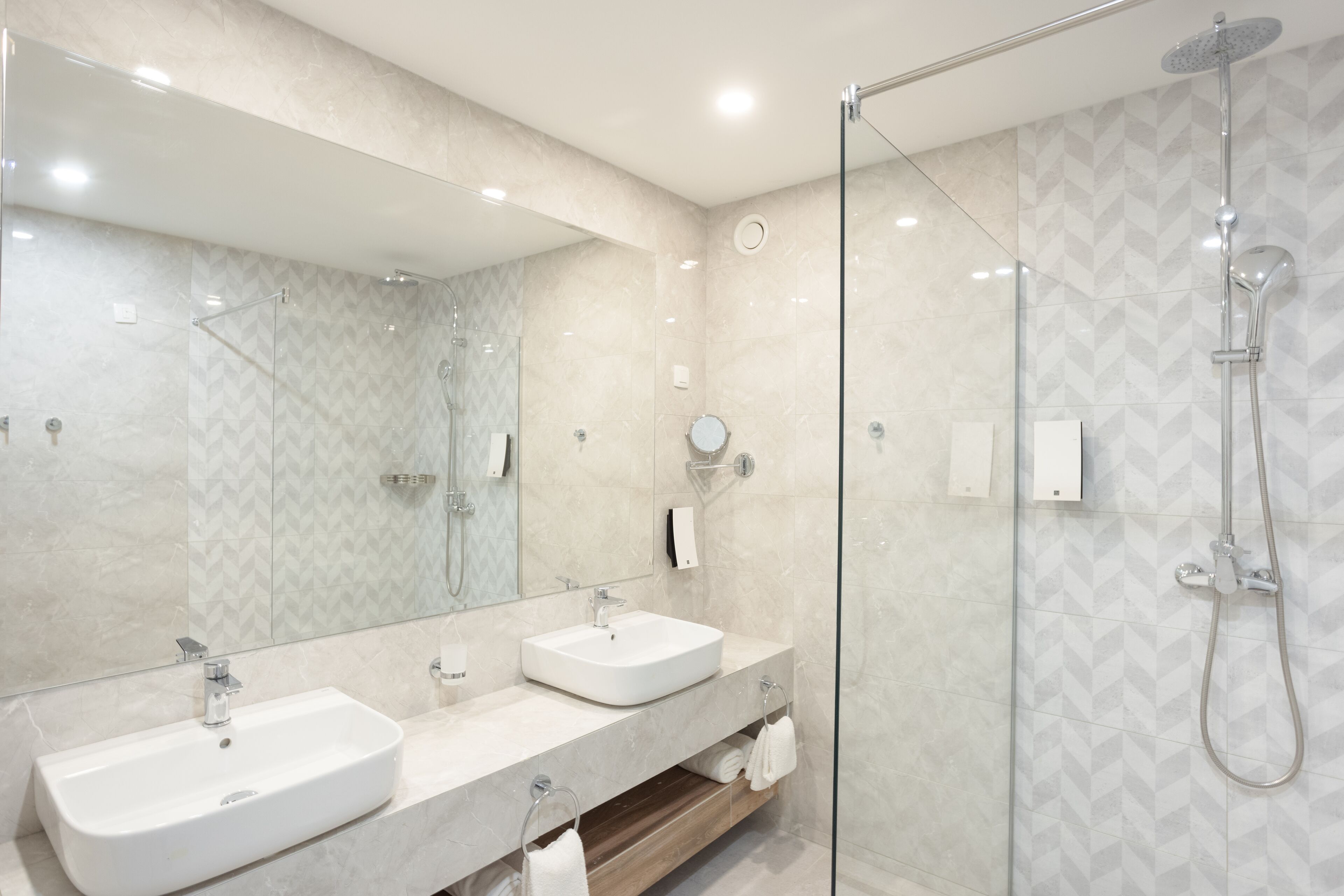 A modern bathroom with two sinks, a glass-enclosed shower, and a large mirror.