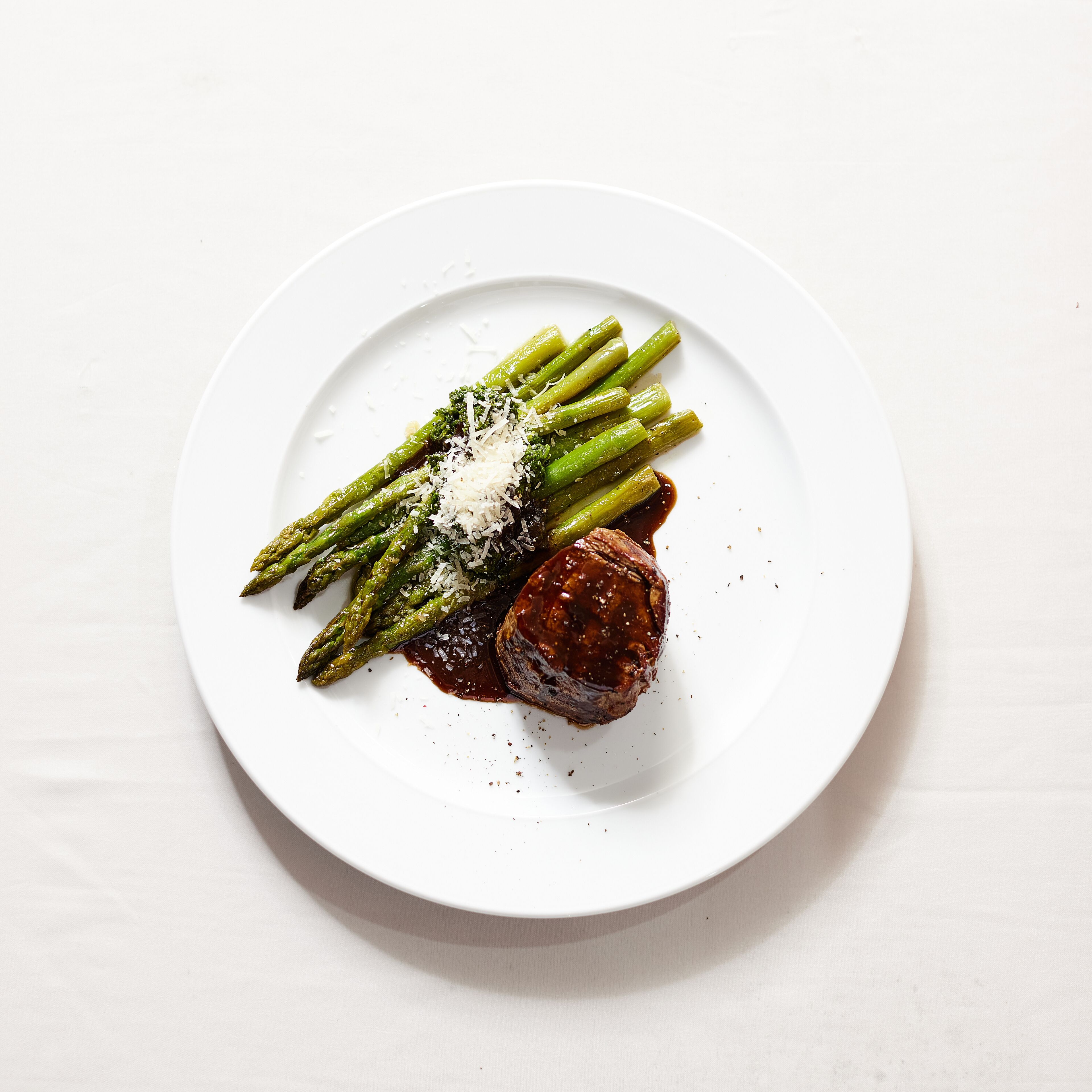 A white plate with asparagus, a piece of meat, and grated cheese.