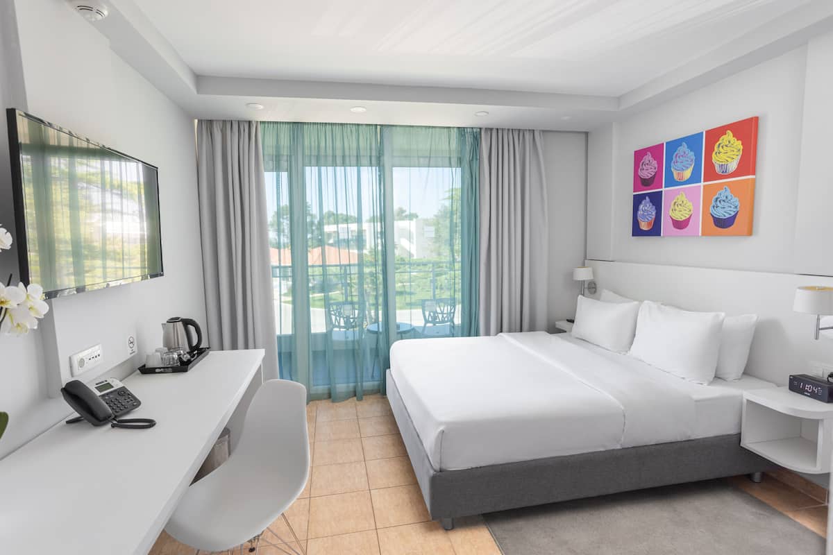 Een hotelkamer met een bed, een bureau met telefoon, een stoel, een televisie en een schilderij aan de muur.