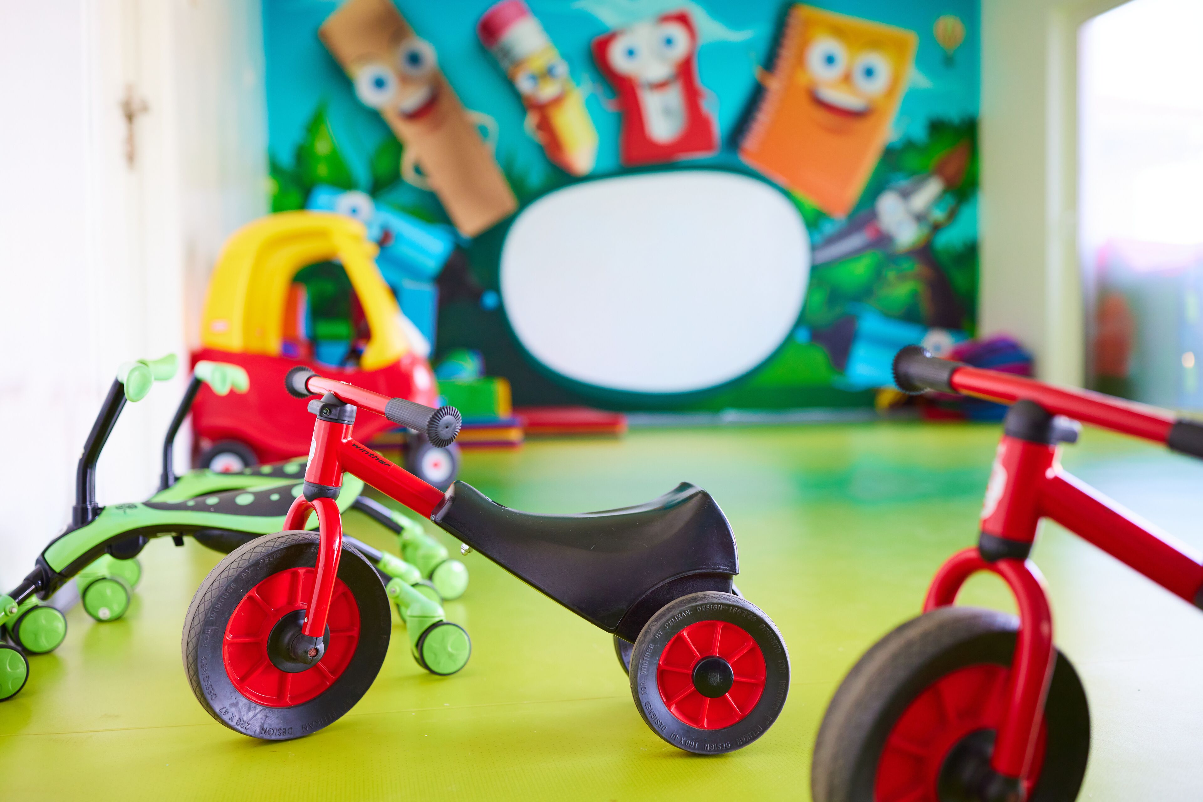 Una habitación con juguetes infantiles de colores, incluyendo una bicicleta roja y un coche de juguete verde.