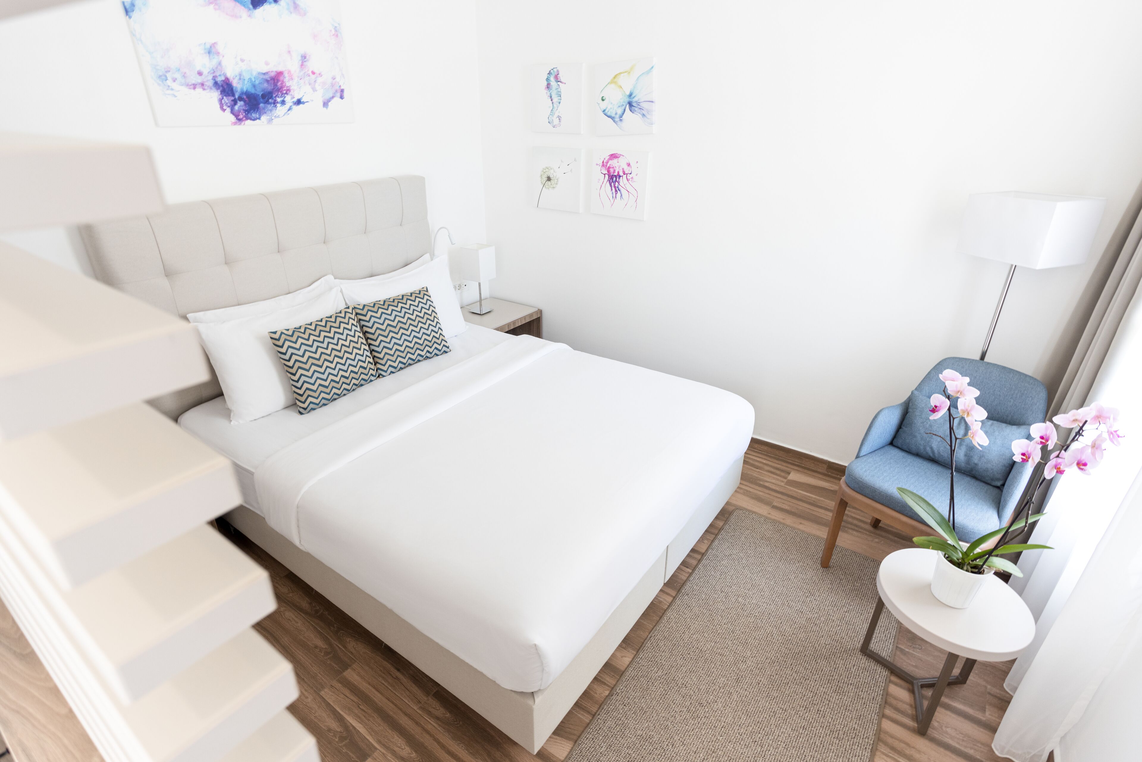 A modern bedroom with a bed, a chair, a nightstand, and a small table with a plant.
