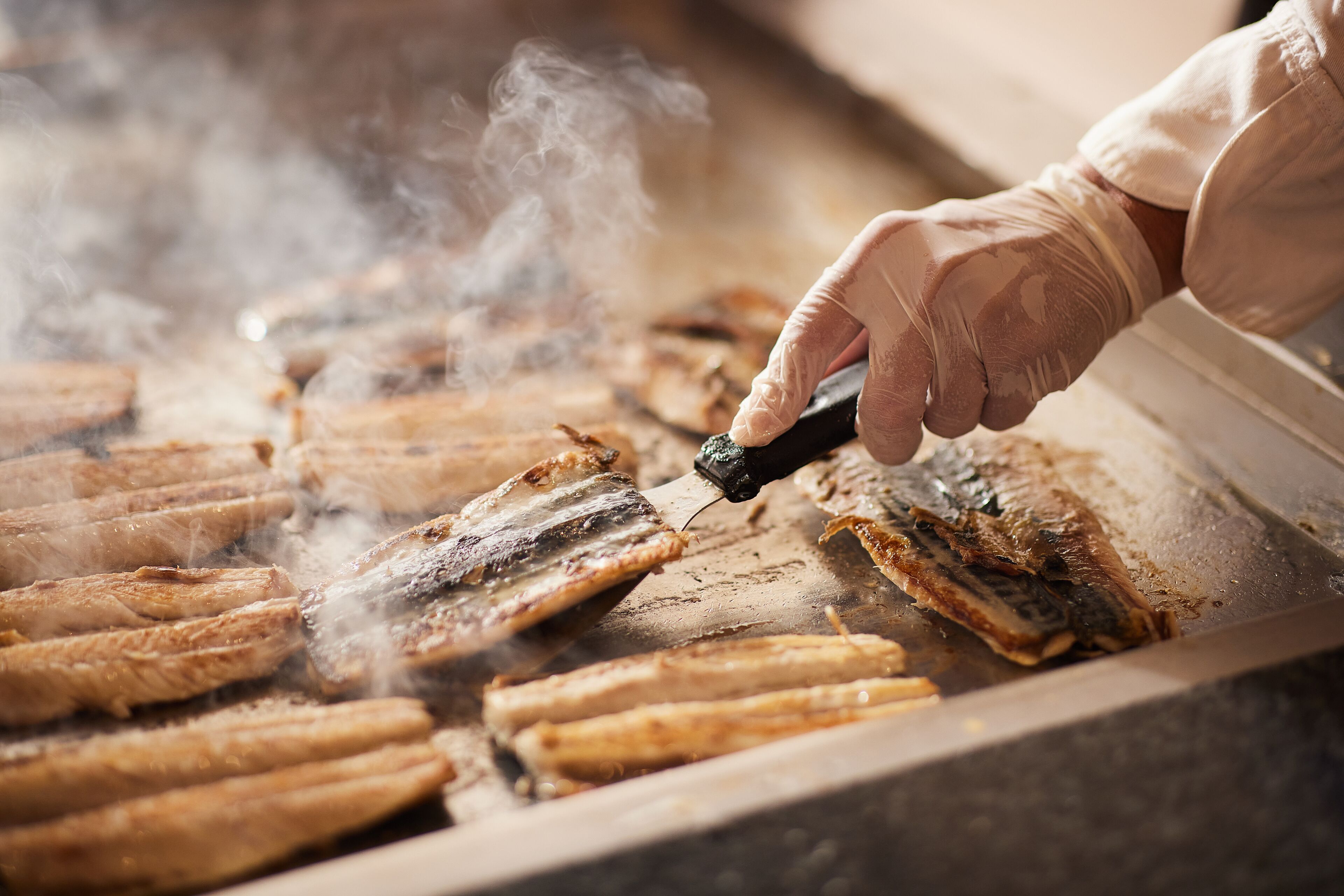A person grilling fish on a flat surface with steam rising.