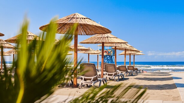 Eine Sitzgelegenheit am Strand mit Reetdachschirmen und Liegestühlen.