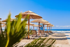 Ett sittområde vid stranden med parasoller av halm och solstolar.
