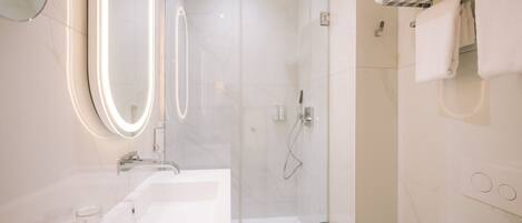 A modern bathroom with a glass-enclosed shower, a large mirror, and a white sink.