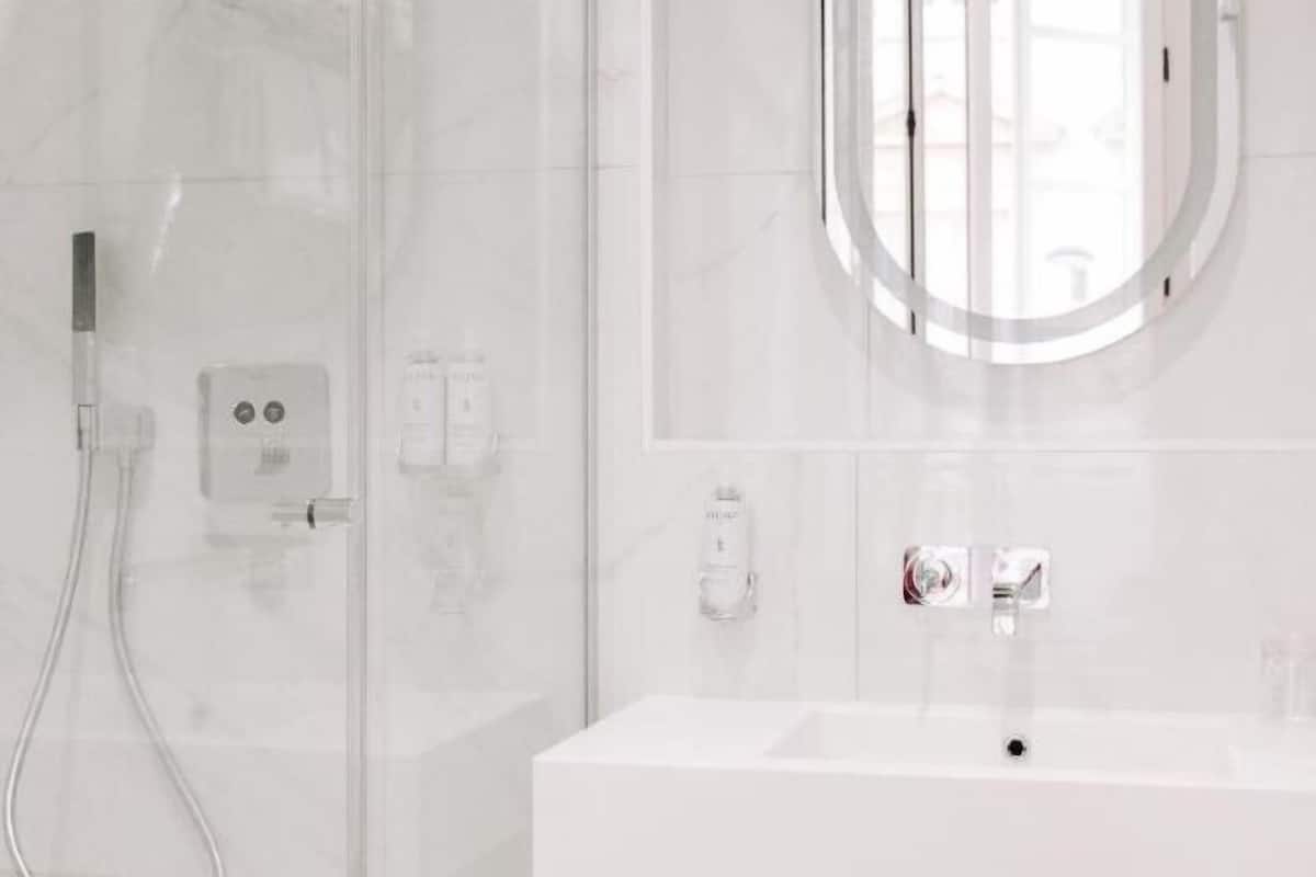 A modern bathroom with a glass shower enclosure, a white sink, and a round mirror.