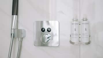 A bathroom with a modern shower control panel, two bottles of Sothys shampoo and conditioner, and a handheld showerhead.