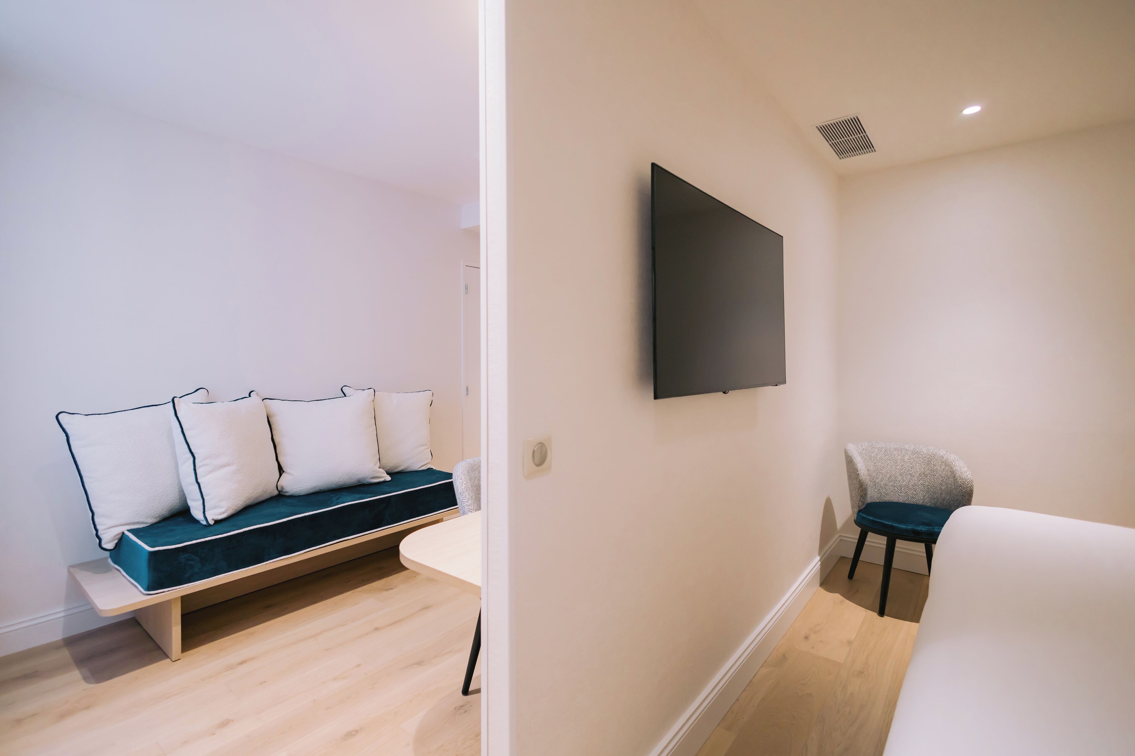 A modern room with a sofa, a chair, a flat-screen TV mounted on the wall, and a wooden floor.