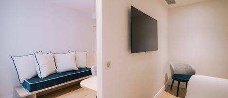 A modern room with a sofa, a chair, a flat-screen TV mounted on the wall, and a wooden floor.