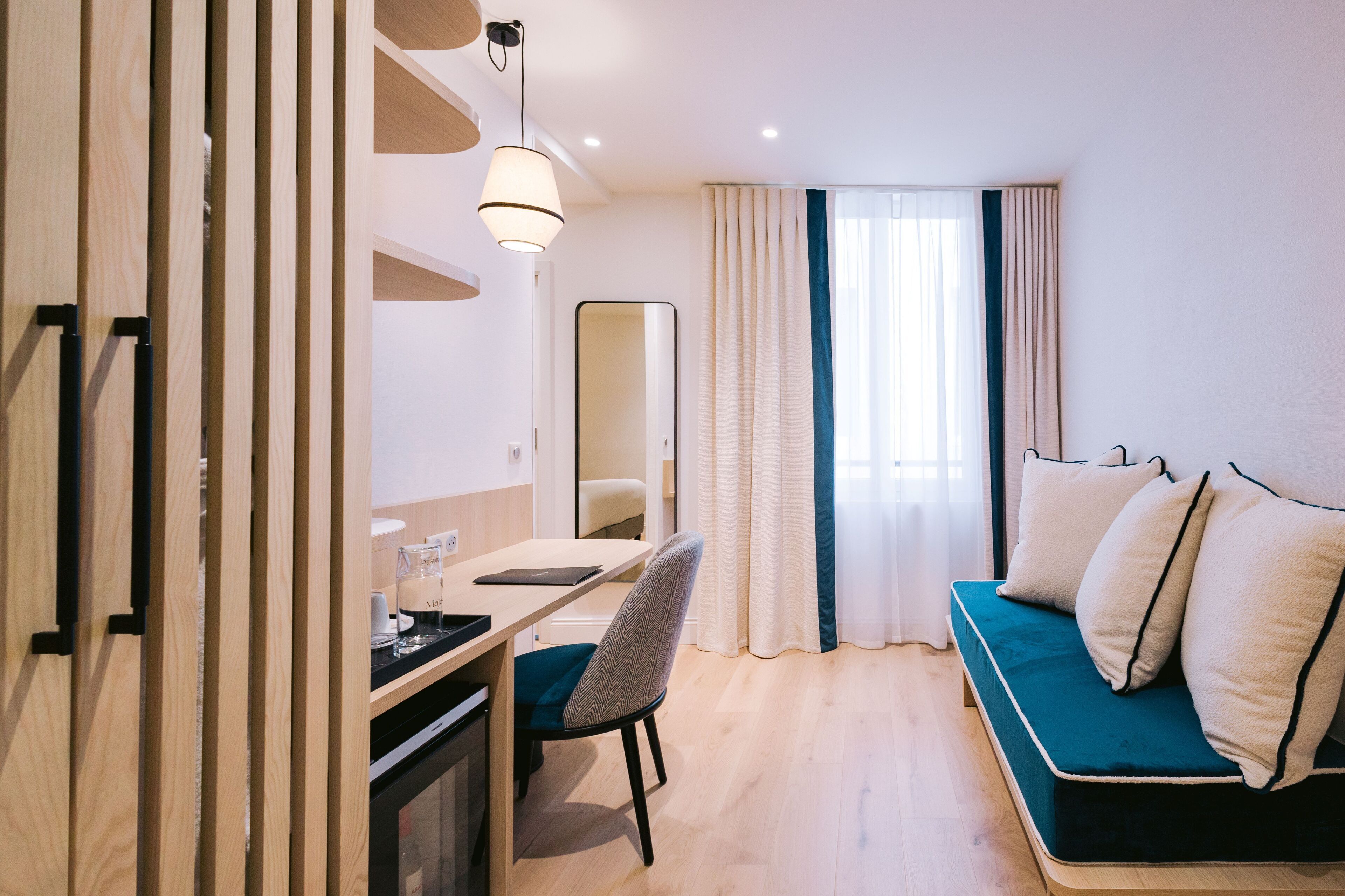 A modern hotel room with a wooden desk, a chair, a sofa, and a large mirror.