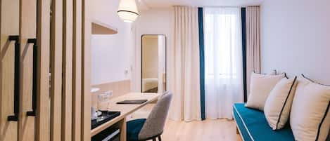 A modern hotel room with a wooden desk, a chair, a sofa, and a large mirror.