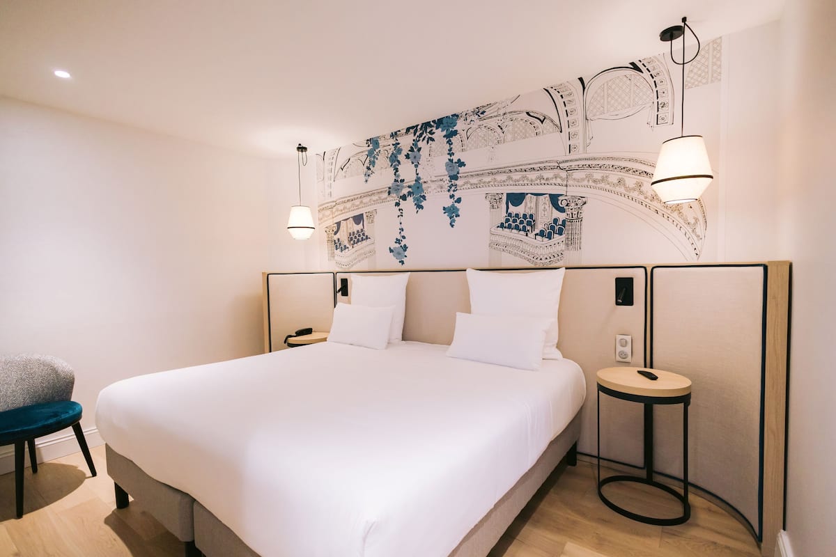 A modern hotel room with a large bed, two bedside tables, and a decorative wall mural.