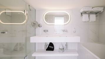 A modern bathroom with a glass shower enclosure, a large vanity with a mirror, and a bathtub.