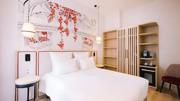 A hotel room with a large bed, a side table, a chair, a wooden bookshelf, and a wall with a decorative map.