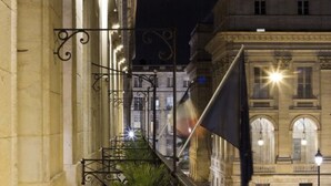 Una vista nocturna de un edificio histórico con arquitectura ornamentada, incluyendo ventanas en arco y un balcón con barandilla de hierro forjado.