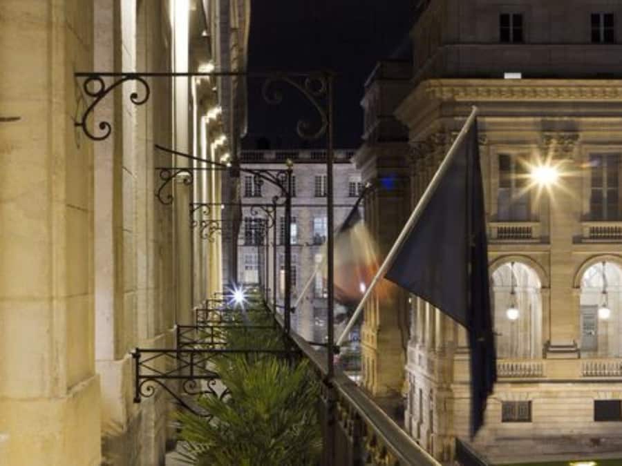 Una vista nocturna de un edificio histórico con arquitectura ornamentada, incluyendo ventanas en arco y un balcón con barandilla de hierro forjado.