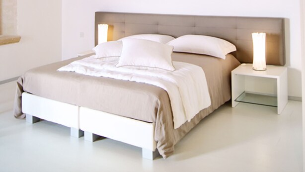 Un dormitorio con techo abovedado de piedra, una cama con ropa blanca y una mesita de noche con lámpara.