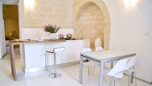 Una cocina moderna con una isla central, taburetes blancos de bar y una mesa de comedor con sillas.