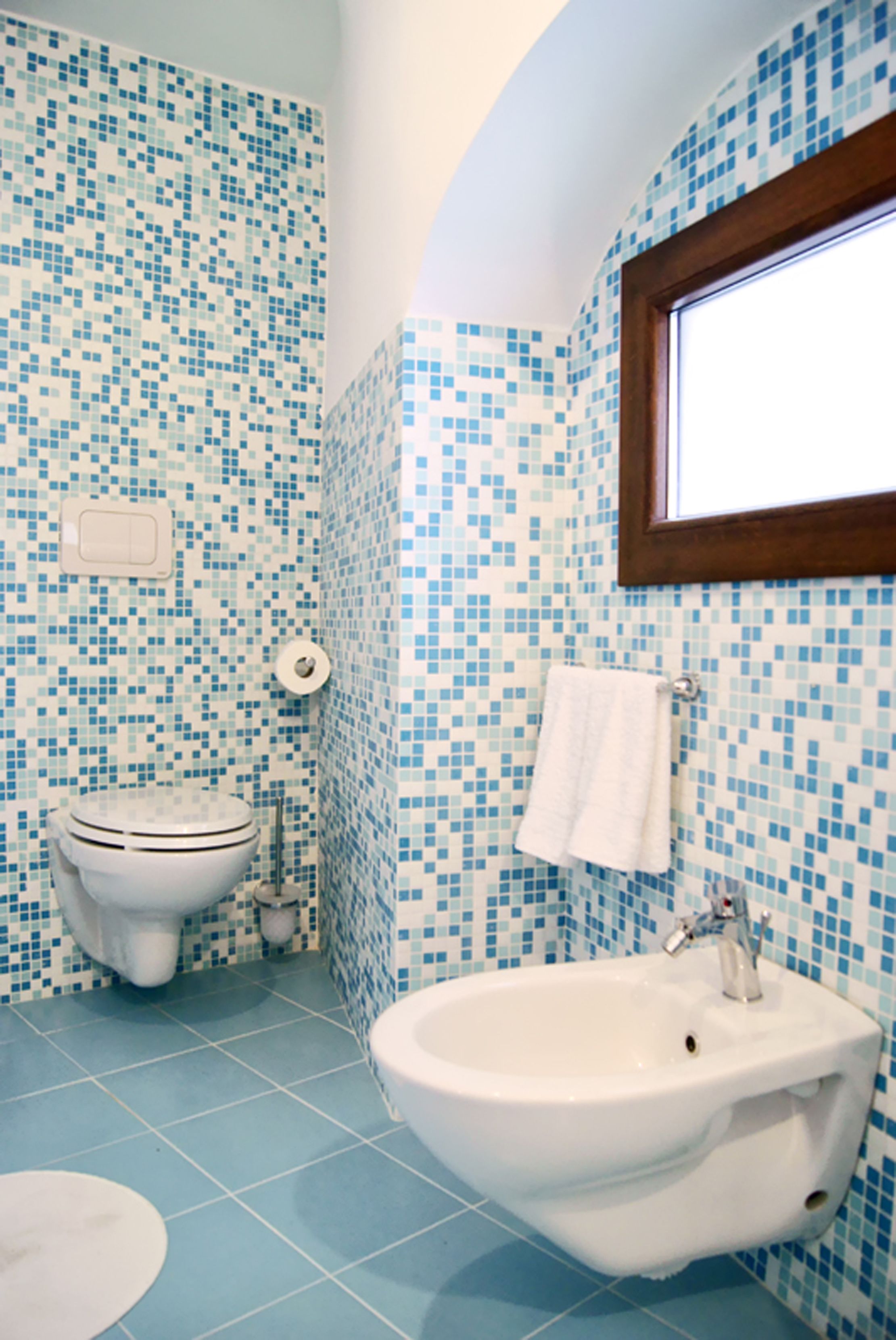 A bathroom with a mosaic tile wall, a toilet, a sink, and a window.