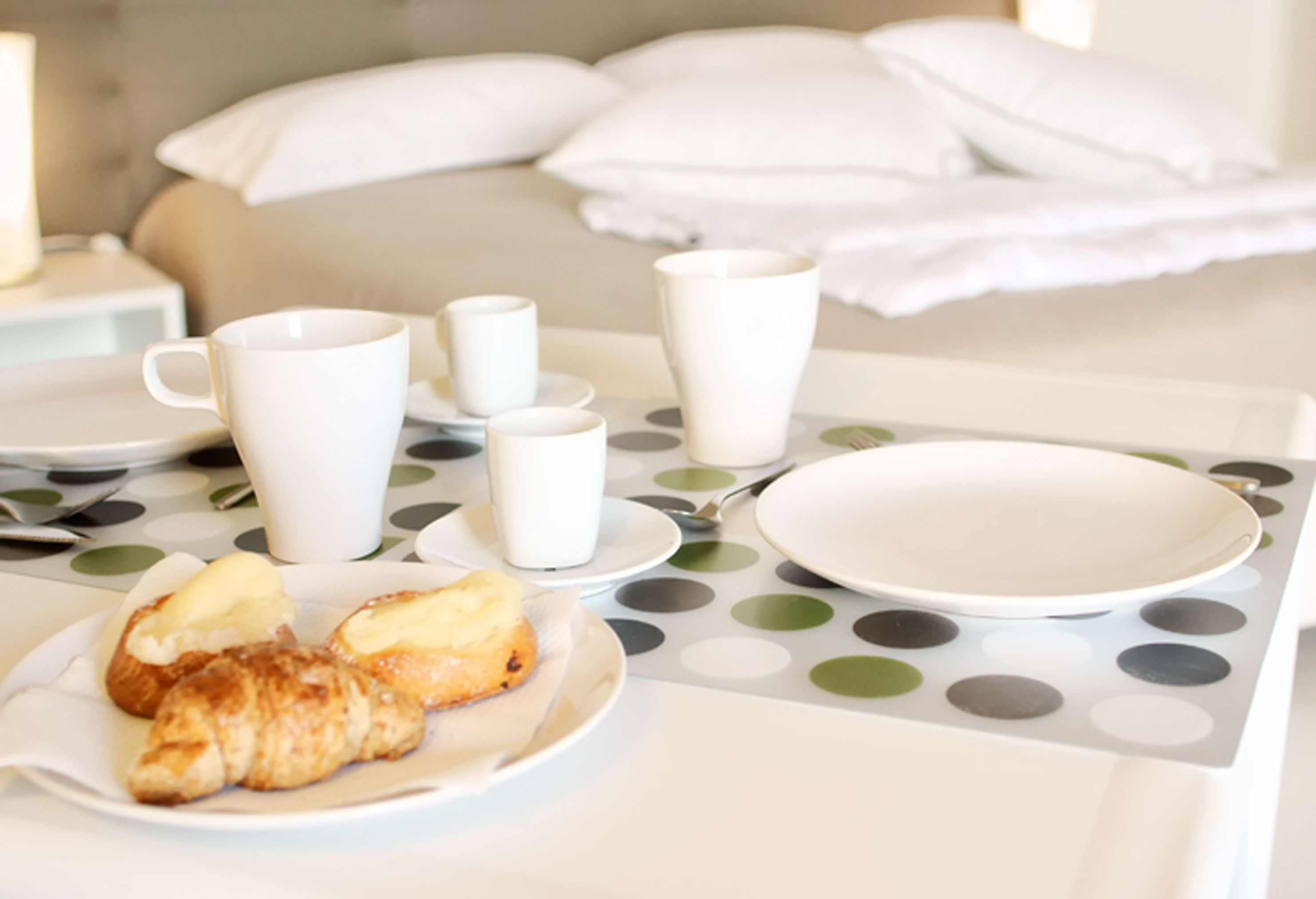 A breakfast setup with croissants and coffee cups on a table with a polka dot tablecloth.