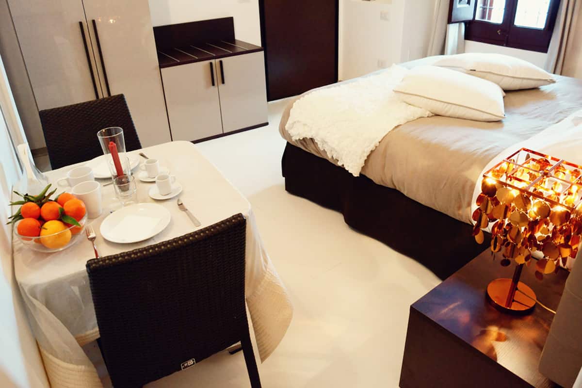 A neatly arranged bedroom with a bed, bedside table, and a dining area with a table set for two.