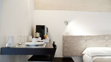 A hotel room with a bed, a bedside table with a lamp, a small table with a coffee maker, and a mirror on the wall.