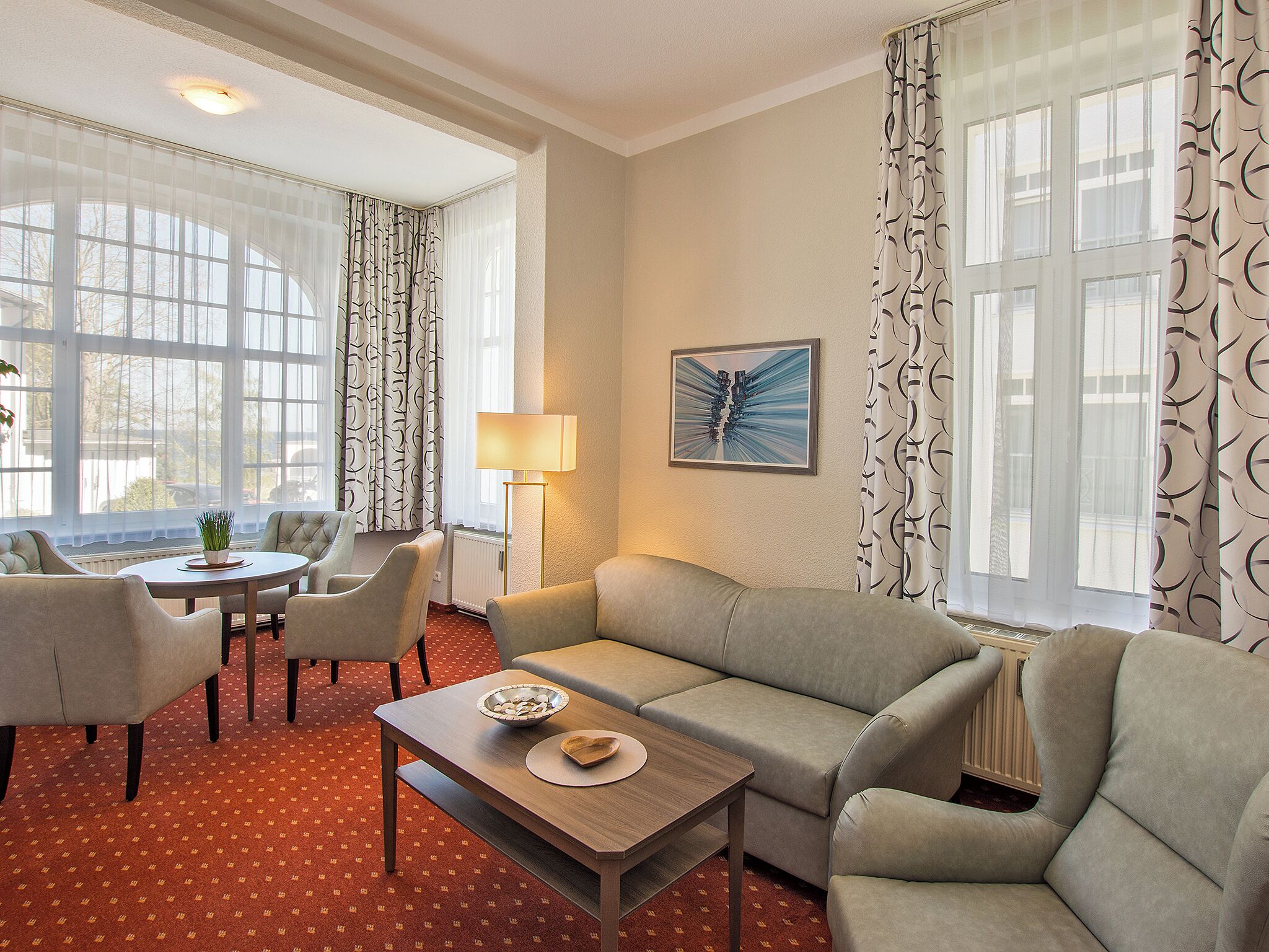 Een hotelkamer met een bank, fauteuils, een eettafel en een lamp.