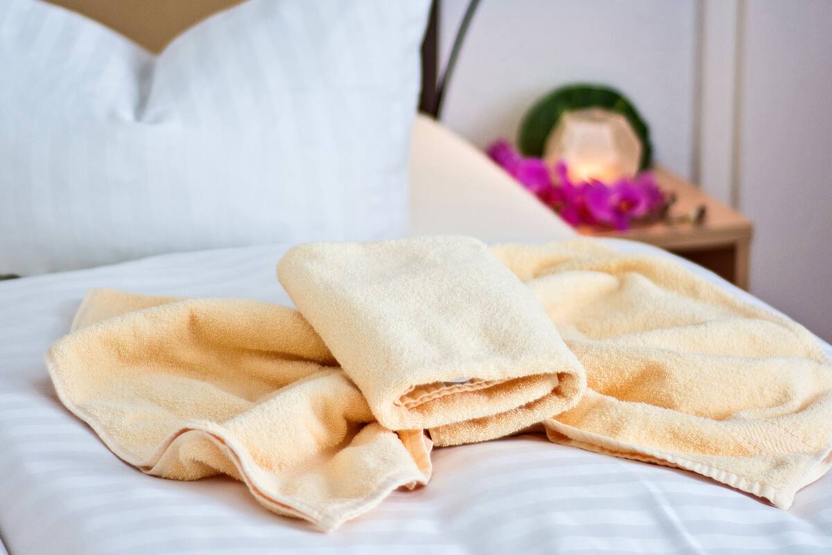 A neatly made bed with folded towels and a bedside lamp.