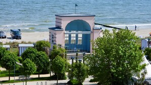 Un bâtiment situé sur la côte, avec une entrée bleue, un drapeau au sommet, et une vue sur la plage et l’océan.