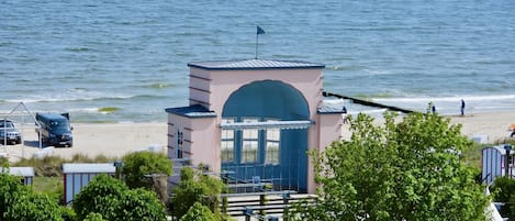 Un edificio costero con una entrada azul, una bandera en la azotea y vistas a la playa y al océano.