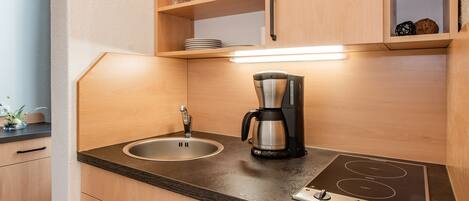 A compact kitchen with a sink, a coffee maker, and a built-in stovetop.