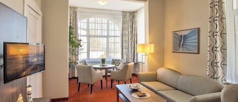 A hotel room with a dining area, a sofa, a TV, and a lamp.