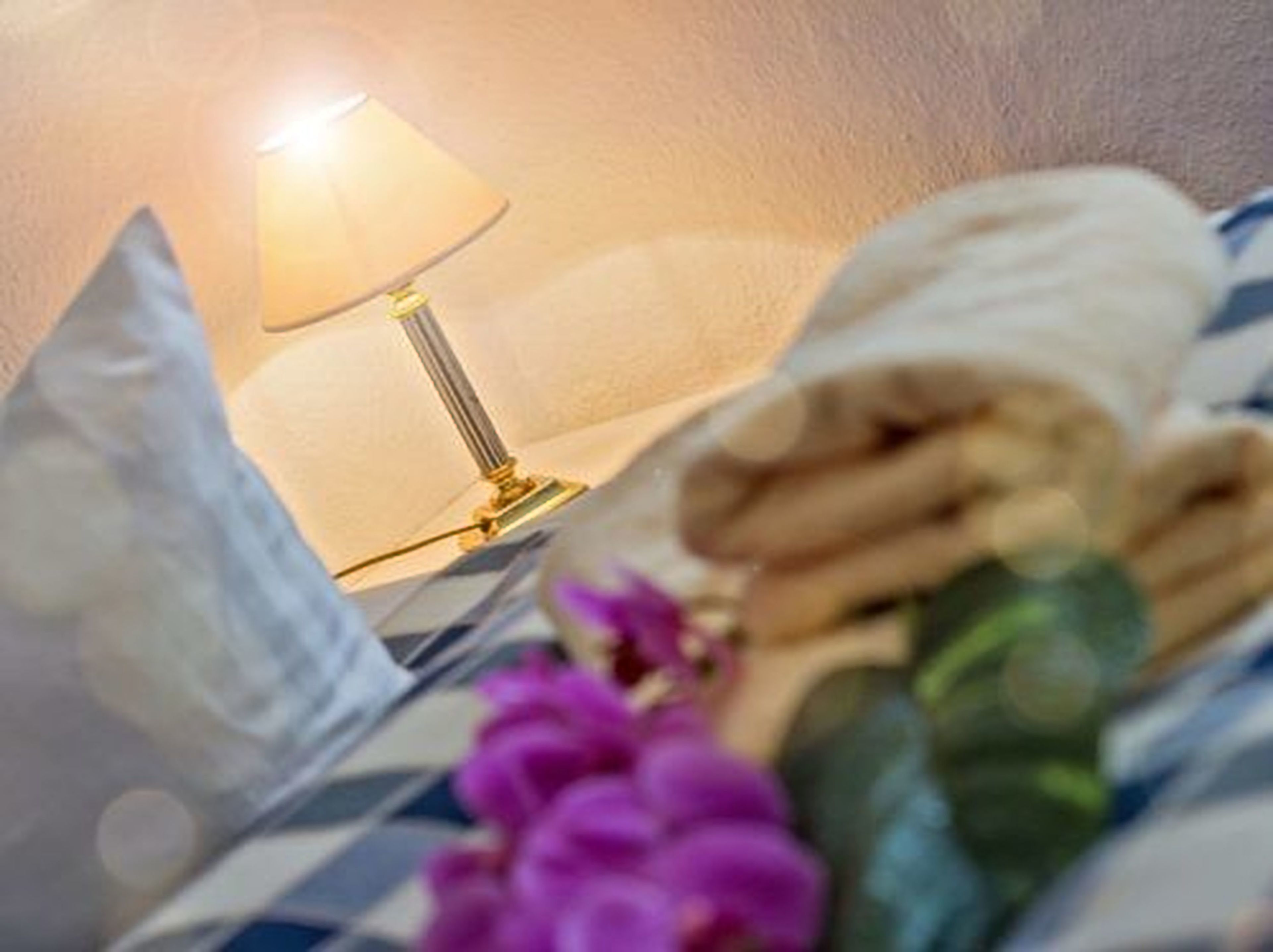 Un lit avec une couvre-lit à carreaux, une serviette enroulée, un oreiller et une lampe.