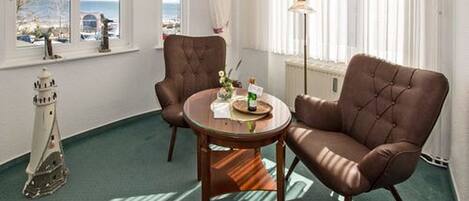 A room with two brown leather armchairs around a small wooden table, a lamp, and a view of the sea through large windows.