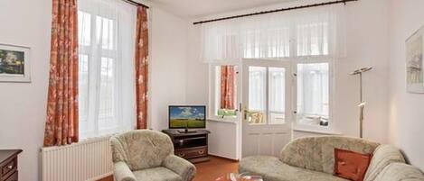 A living room with a sofa, armchair, and a coffee table with a bowl. There is a television on a stand and a radiator.