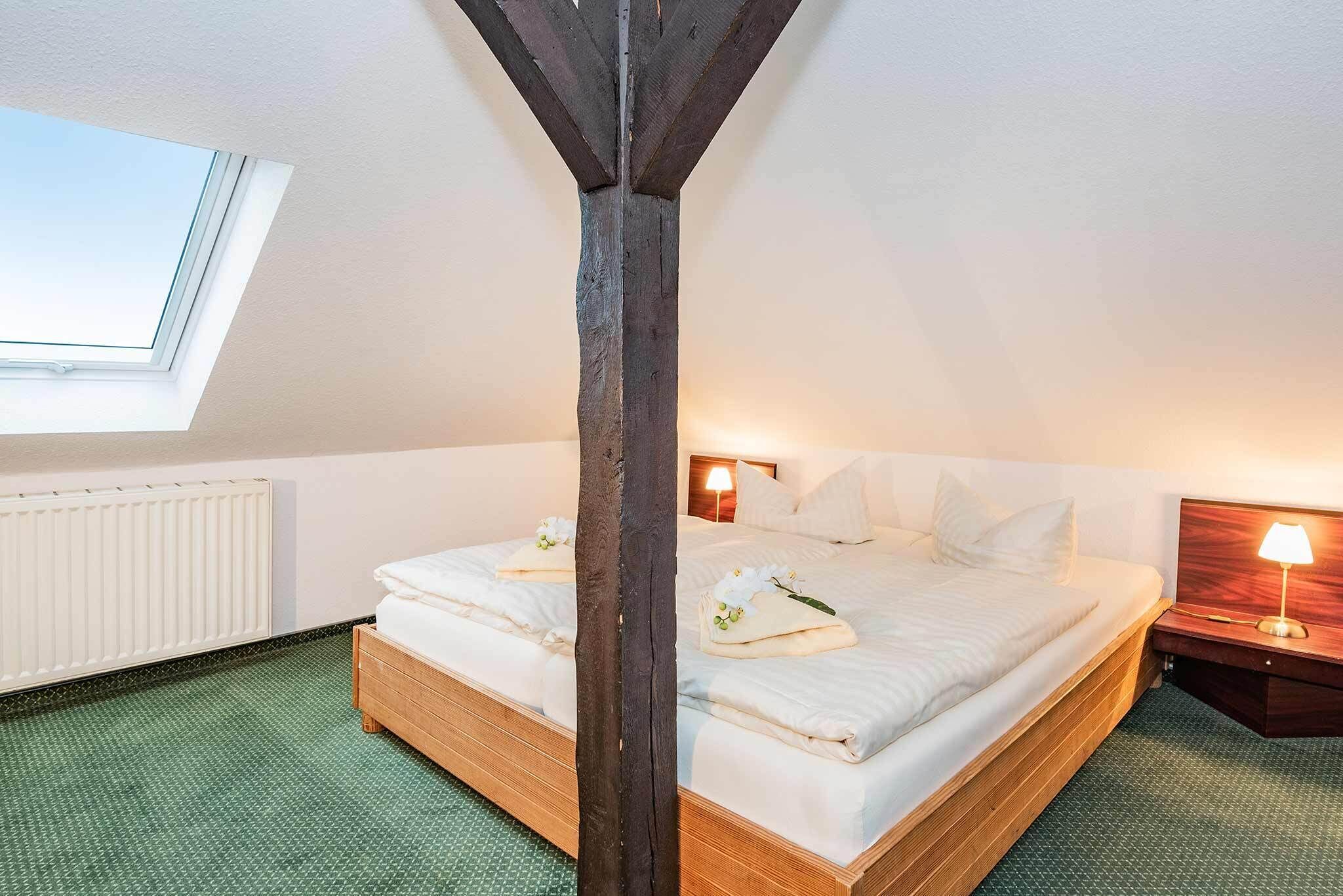A room with a wooden bed, a skylight, a radiator, and a nightstand with a lamp.