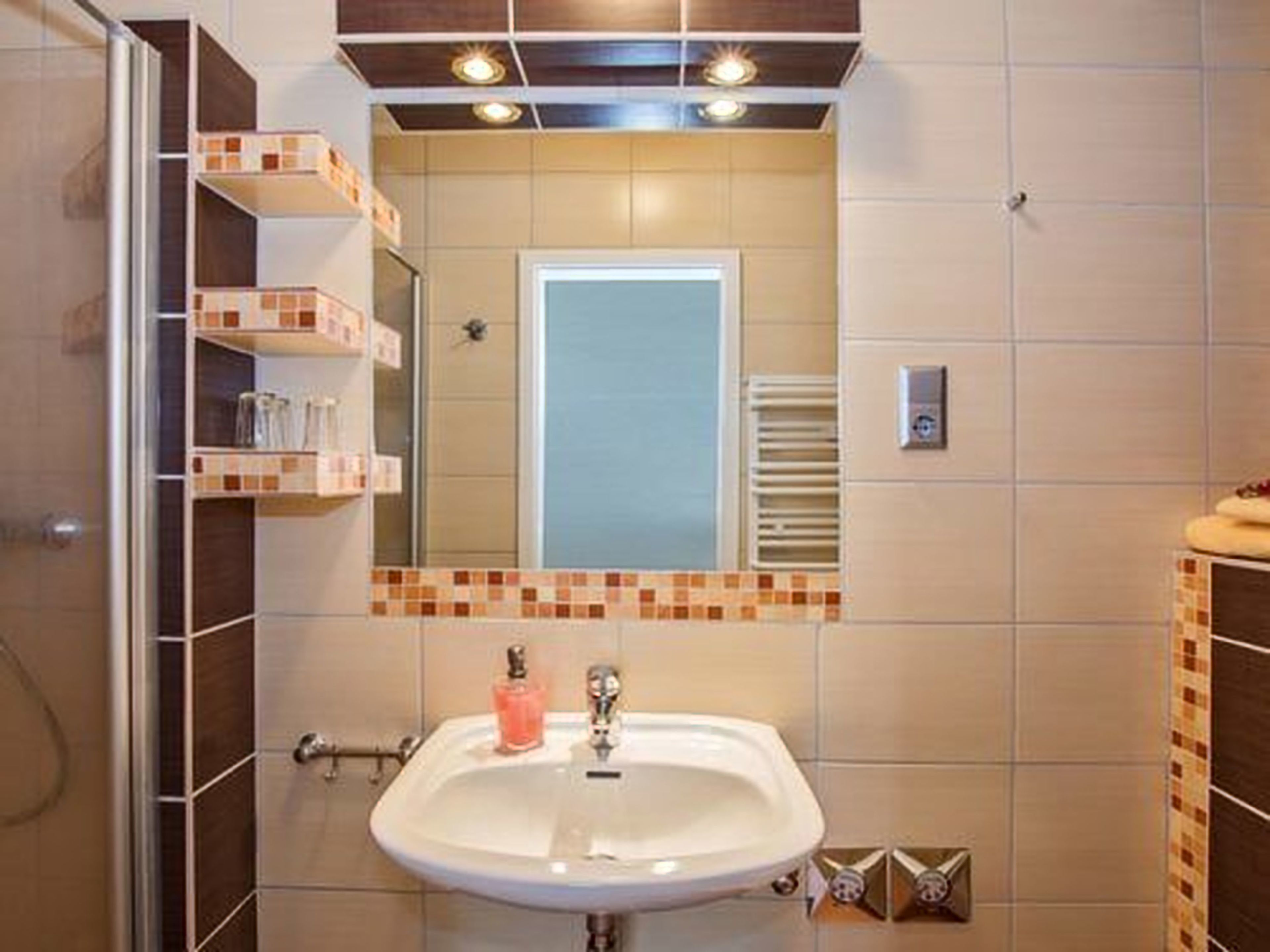 Un bagno con lavandino bianco, specchio e parete rivestita in piastrelle.