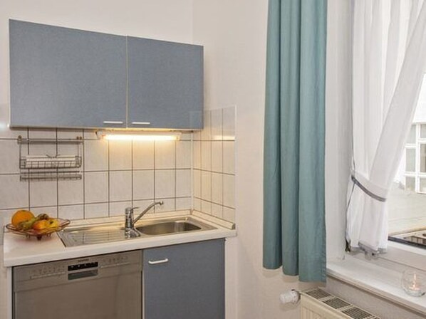 A compact kitchen with a dishwasher, a sink, and a fruit bowl on the counter.