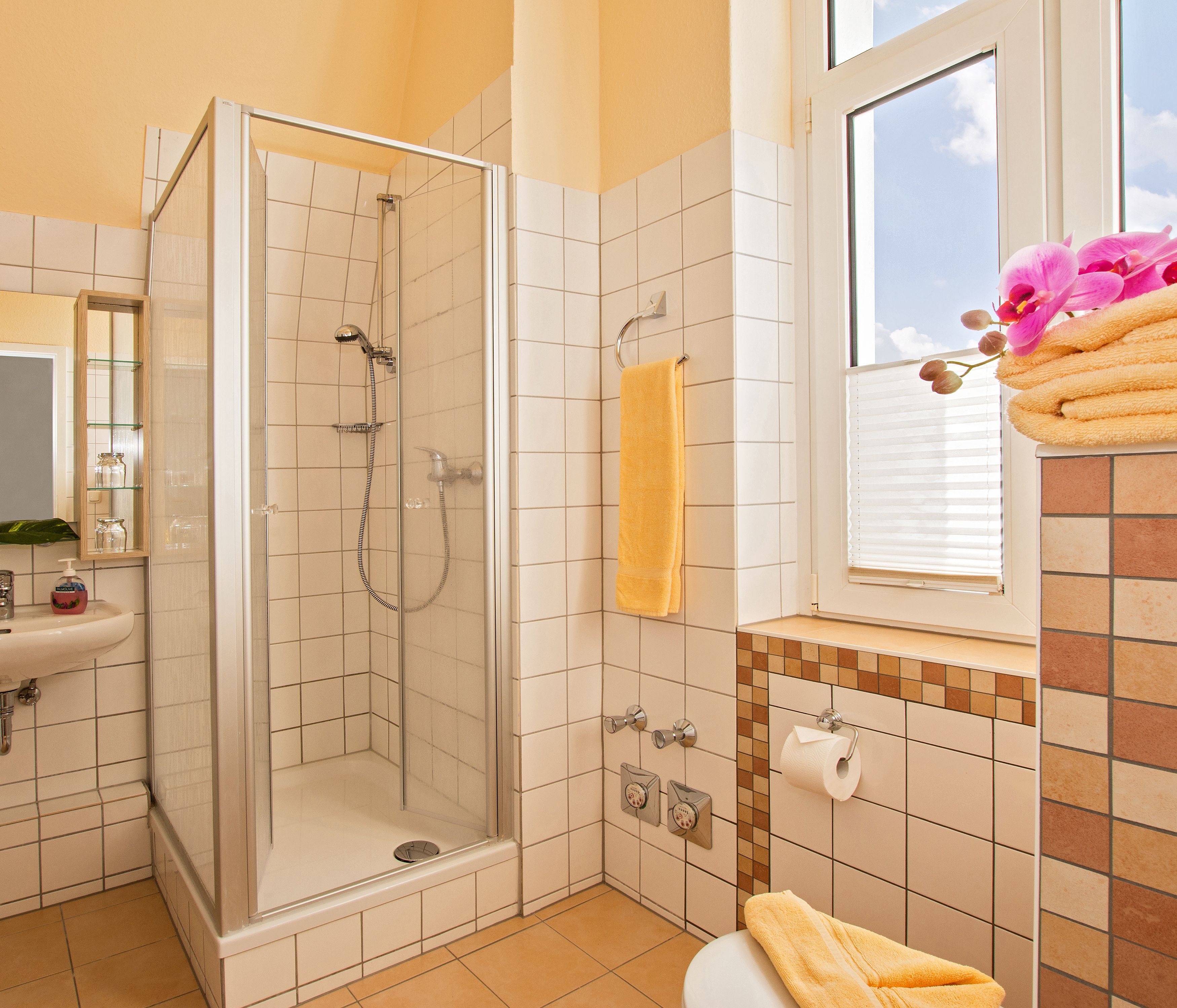 A bathroom with a glass-enclosed shower, a sink, a toilet, and a window with a view of the sky.